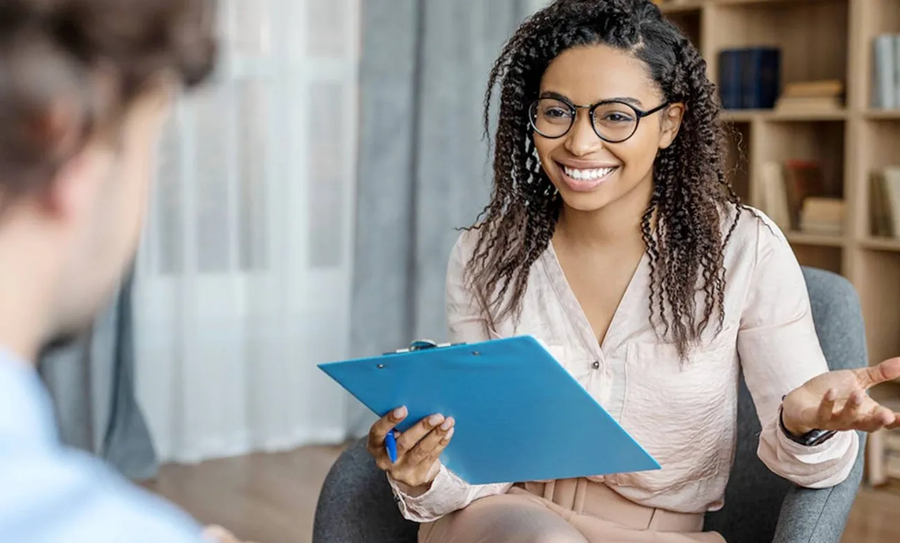 A life coach holding a clipboard and pen while talking to a client in a cozy office setting.